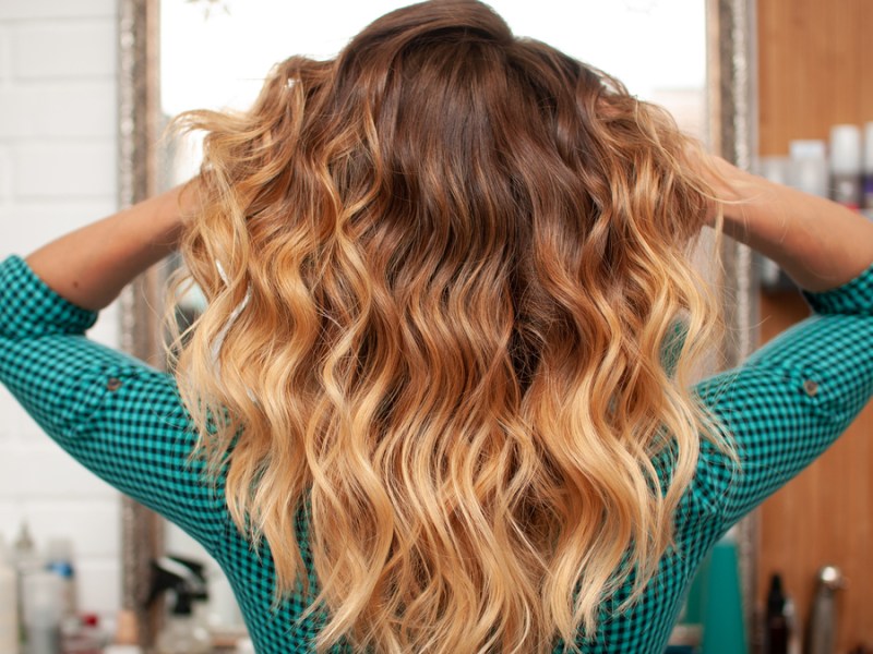 Von hinten fotografiert: Eine Frau mit Ombre-Strähnen in den Haaren wuschelt in ihre Haare einmal durch.