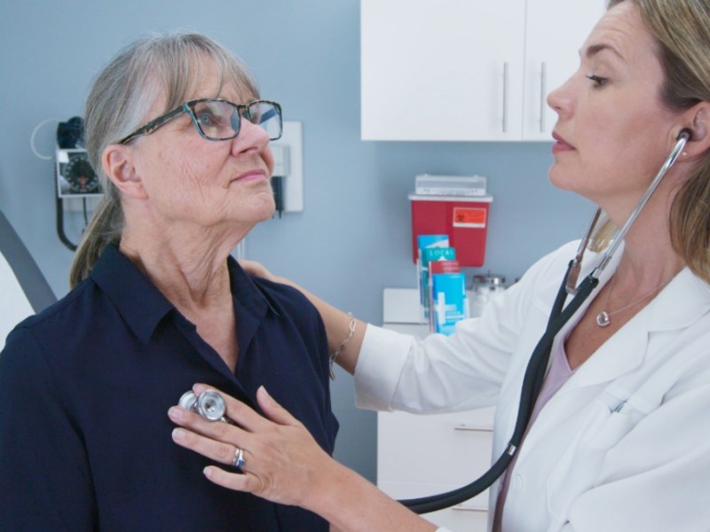 Eine junge Ärztin hört mit einem Stethoskop eine ältere Patientin ab.