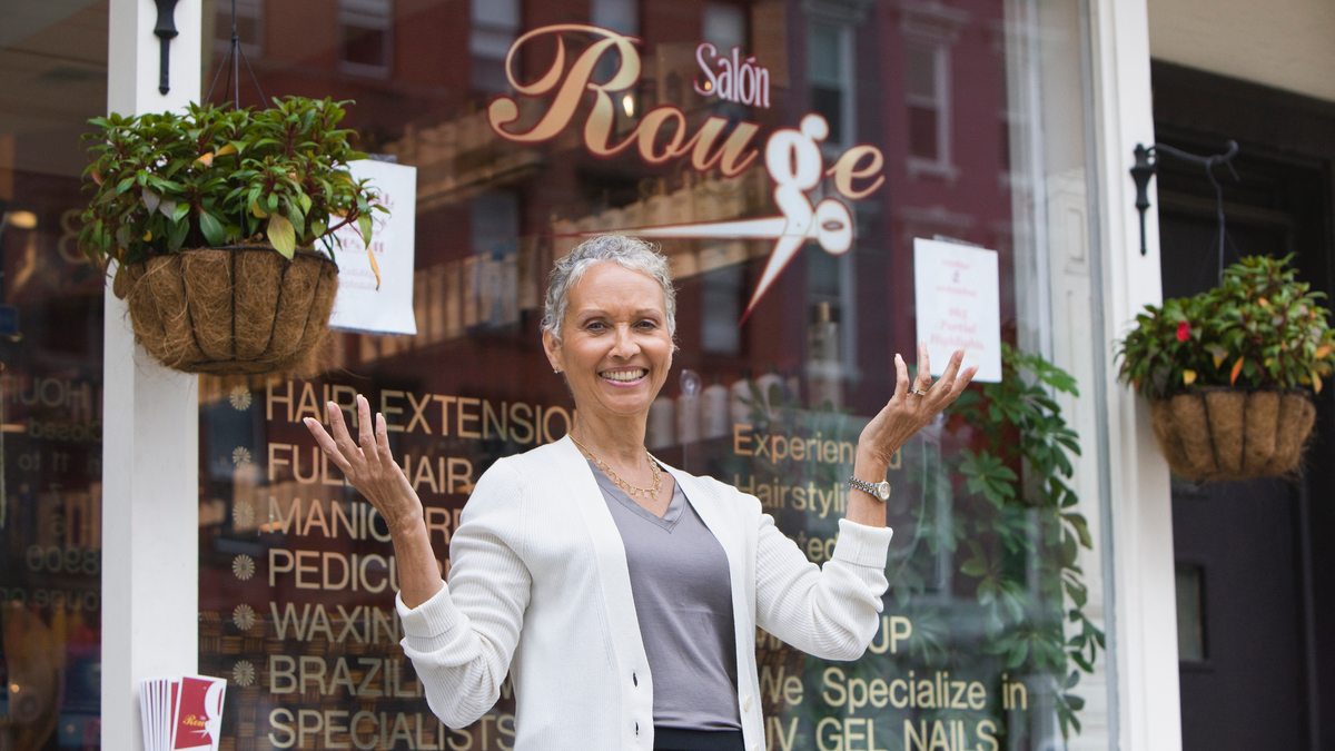 Eine Frau mit kurzen grauen Haaren steht vor einem Friseur-Salon.