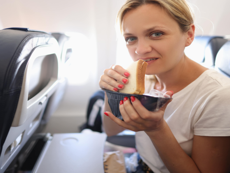 Frau guck fragend in die Kamera während sie ein Sandwich isst.