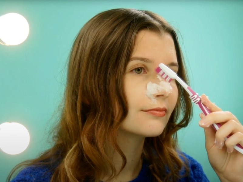 Eine junge Frau reinigt sich die Haut mit einem Backpulver-Peeling und einer Zahnbürste.