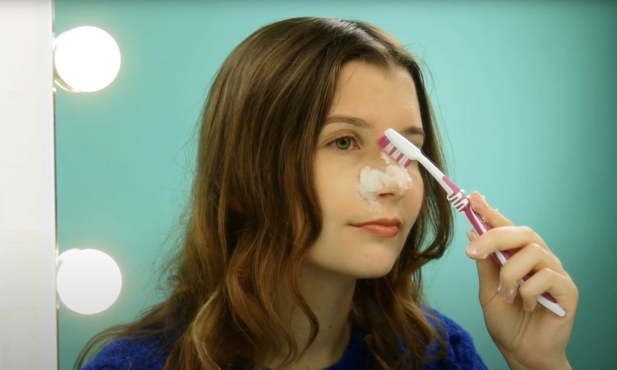 Eine junge Frau reinigt sich die Haut mit einem Backpulver-Peeling und einer Zahnbürste.