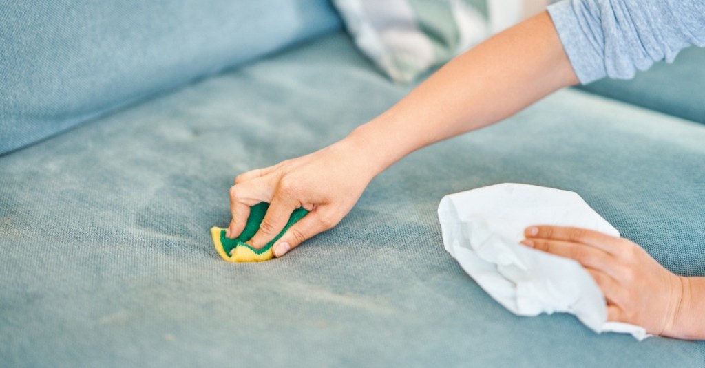 Polstermöbel reinigen: Eine Frau reinigt ein Sofa mit einem Schwamm.