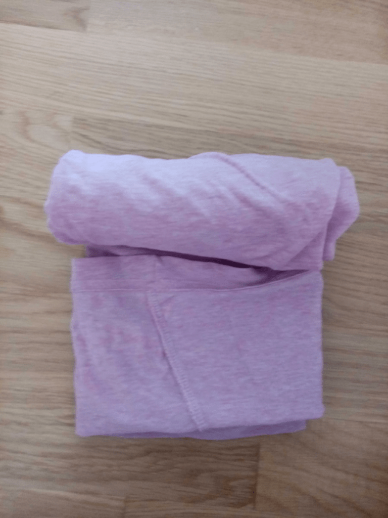 Ein gerolltes, rosa T-Shirt liegt auf dem Boden.