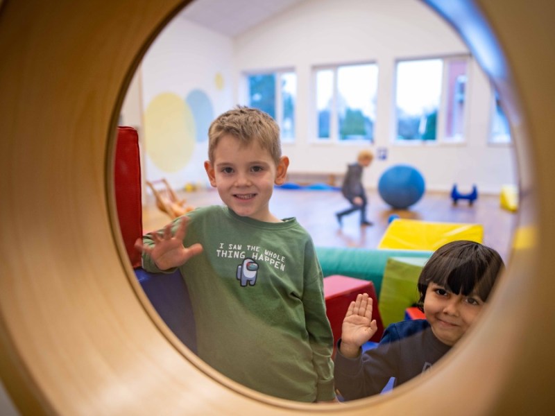 Kinder winken durch ein Bullauge im Kindergarten