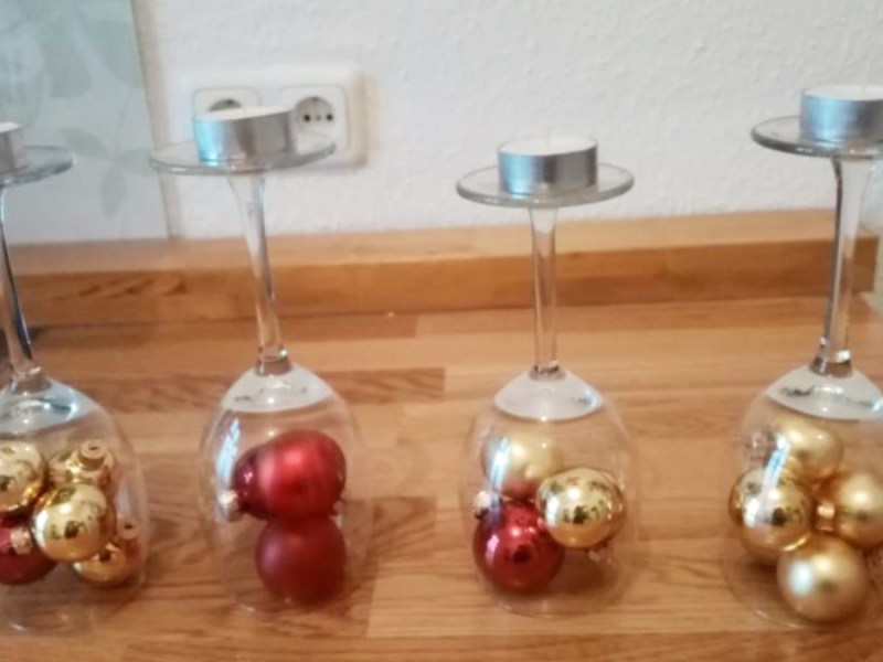 Ein Weihnachtskranz-Gesteck aus Christbaumkugeln in umgedrehten Weingläsern.