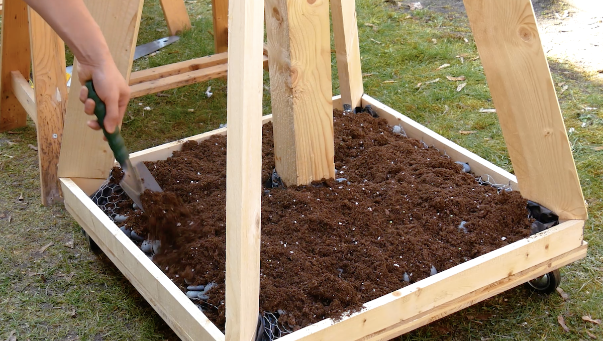 Steine und Blumenerde werden in die Basis eines vertikalen Gartens gelegt.