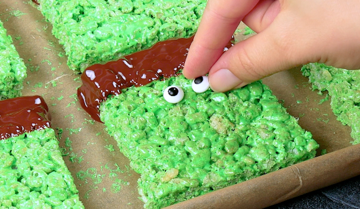 Ein grüner Rice-Krispie-Taler wird mit Zuckeraugen und Schokolade verziert.