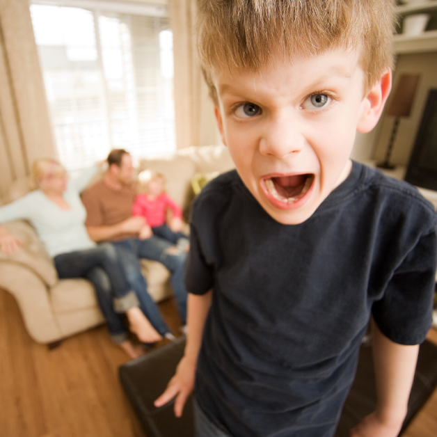 Im Vordergrund schreit ein Junge, wÃ¤hrend seine Eltern und ein Geschwisterkind im Hintergrund auf einem hellen Sofa sitzen