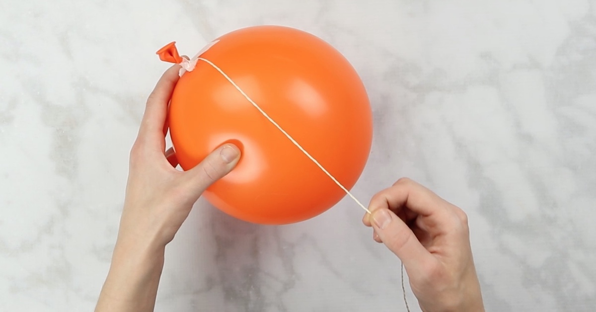 Ein orangefarbener Ballon wird mit Schnur umwickeln.