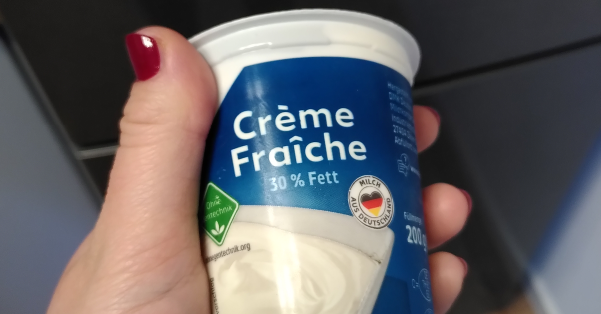 Eine Hand hÃ¤lt einen Becher Creme Fraiche.