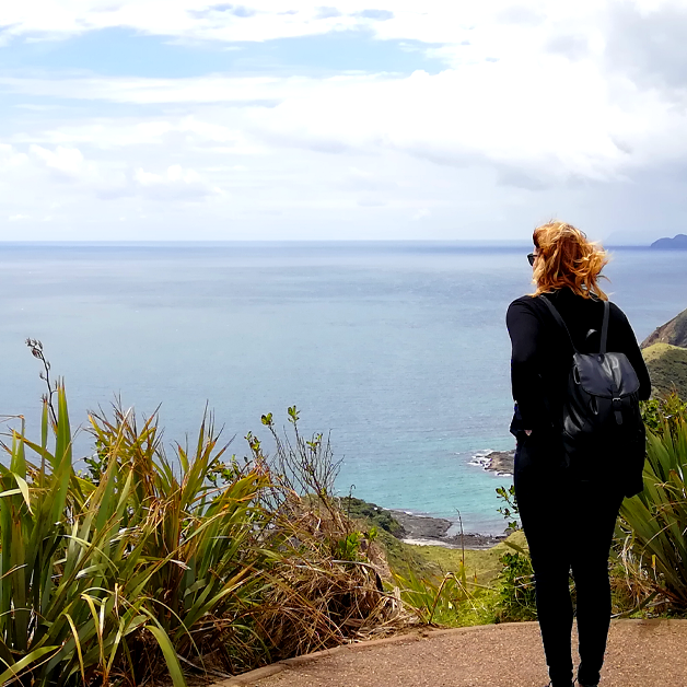 Eine Frau steht an einem Aussichtspunkt und schaut auf der Meer vor ihr.