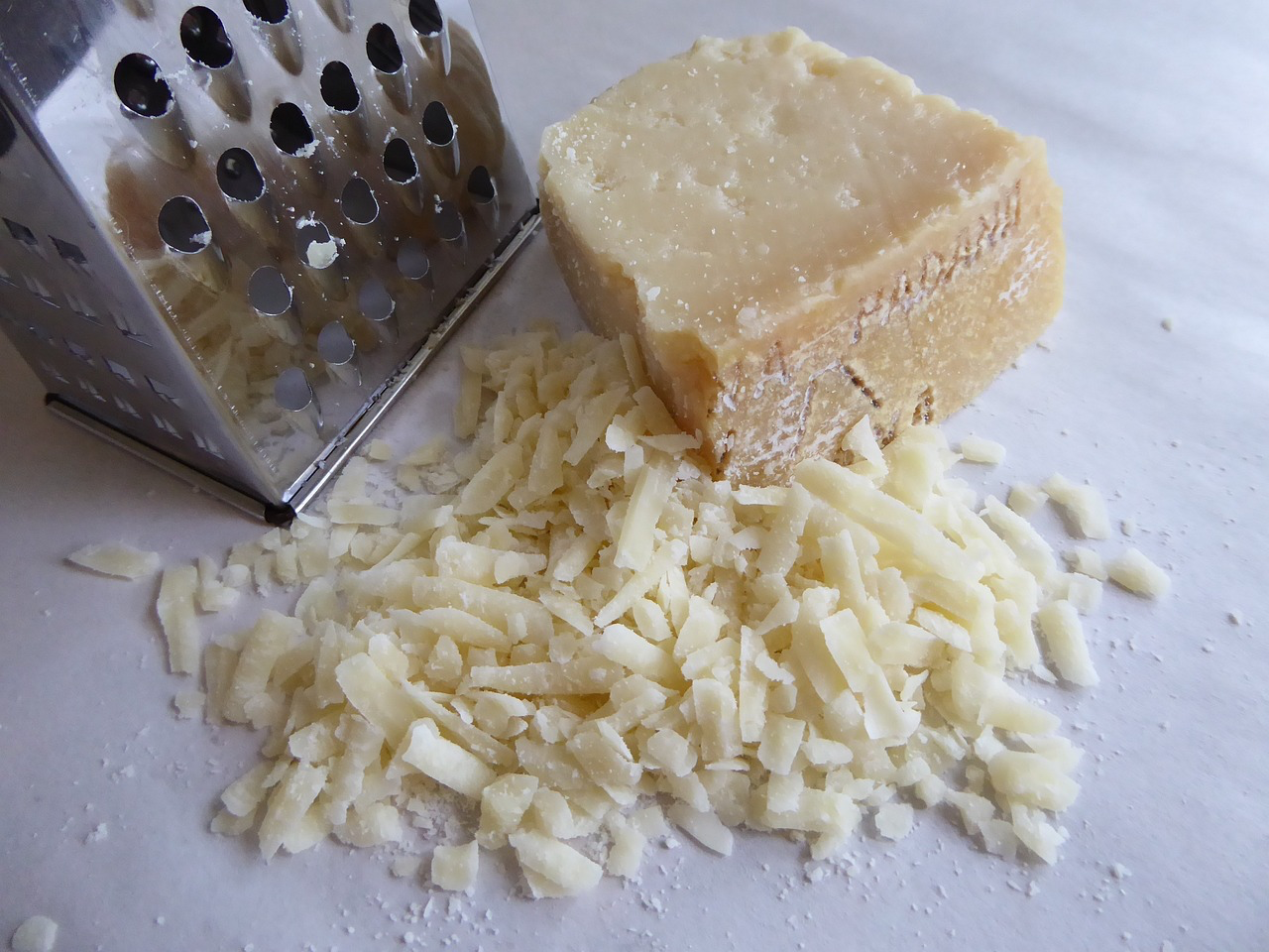 Eine Reibe, ein Stück Parmesan und geriebener Parmesankäse. Parmesan ist im Stück länger haltbar und besser zu lagern.