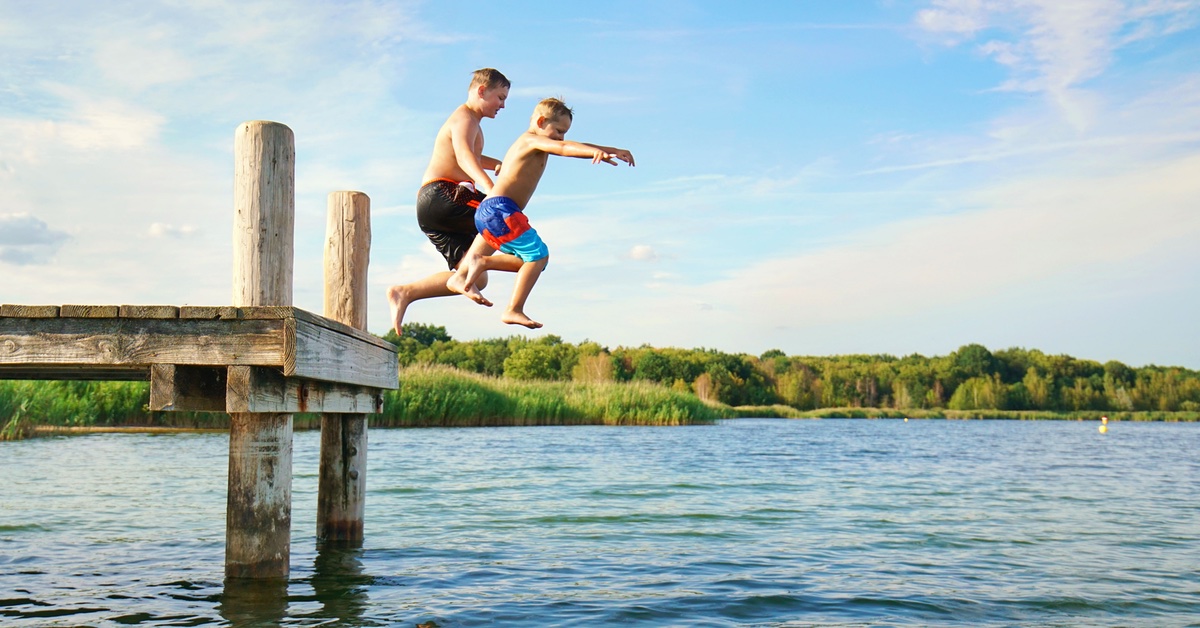 Zwei Personen springen von einem Steg ins Wasser.