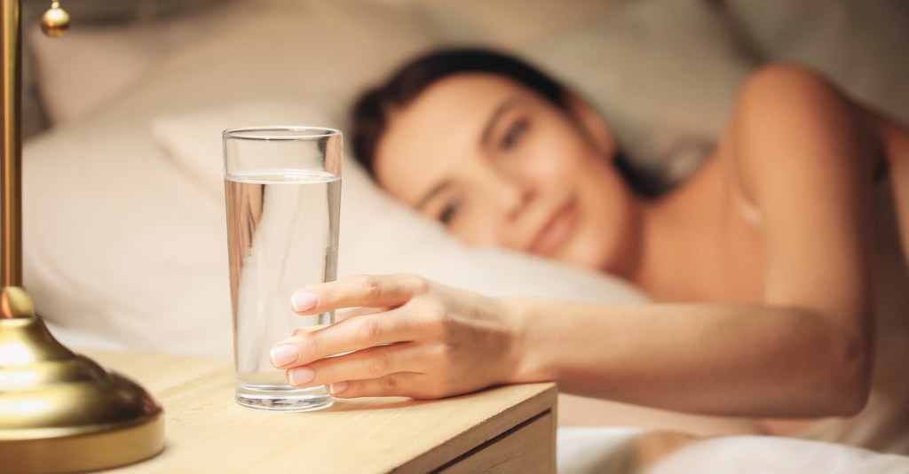 Frau greift zu einem Glas Wasser auf dem Nachttisch.