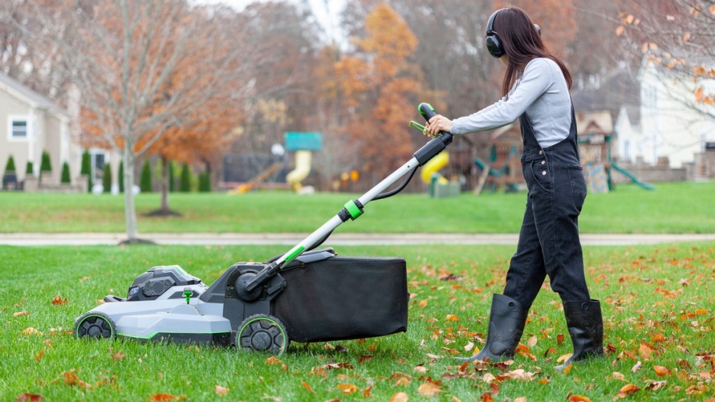 Eine Frau mäht Herbstlaub auf dem Rasen.