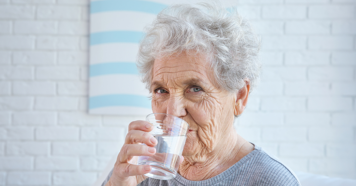 Alte Frau trinkt ein Glas Wasser.