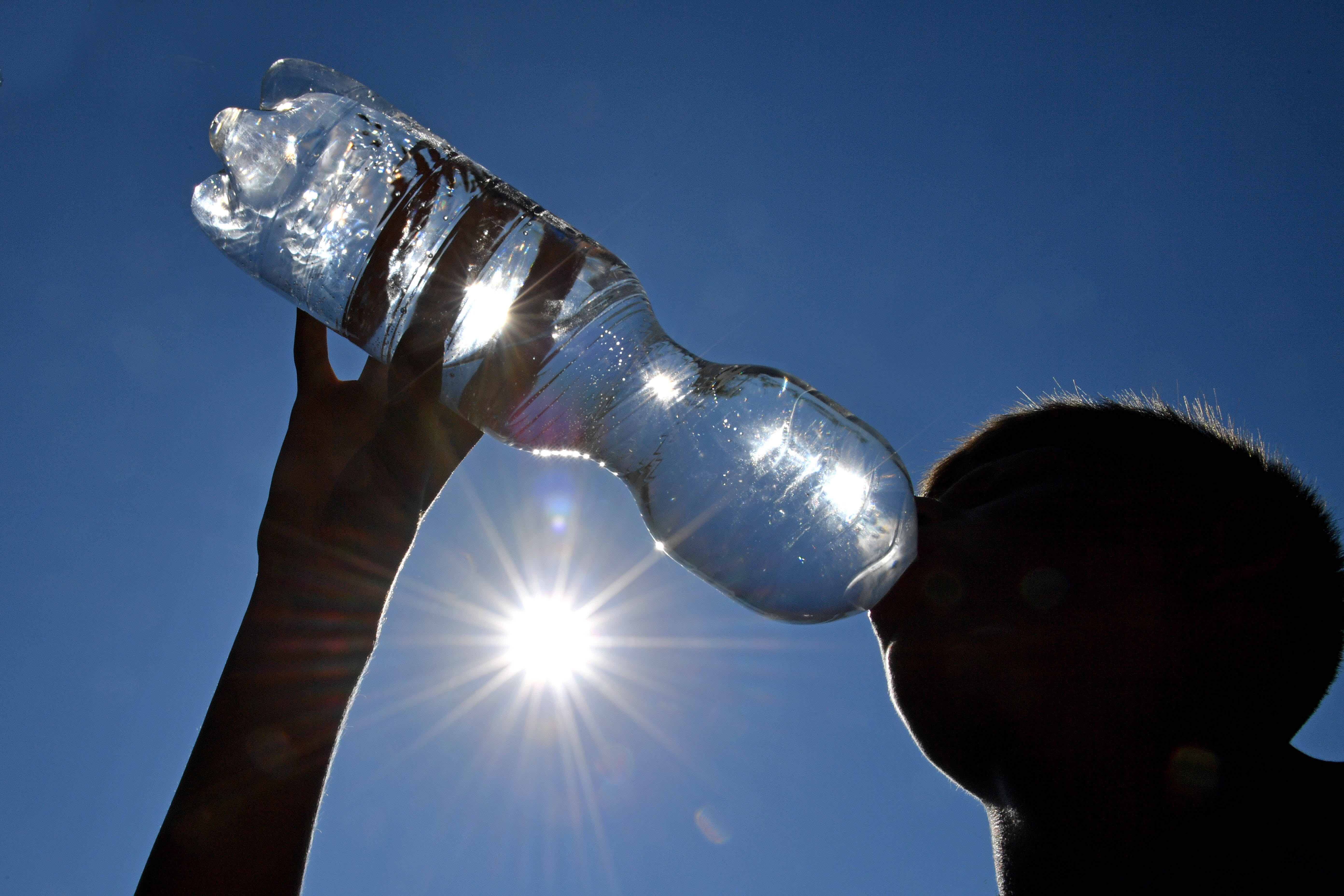 Eine Person trinkt aus einer Wasserflasche während die Sonne scheint.