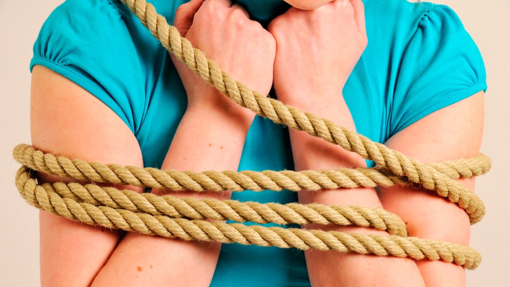 Eine Frau in einem hellblauen T-Shirt ist mit einem dicken Seil gefesselt.