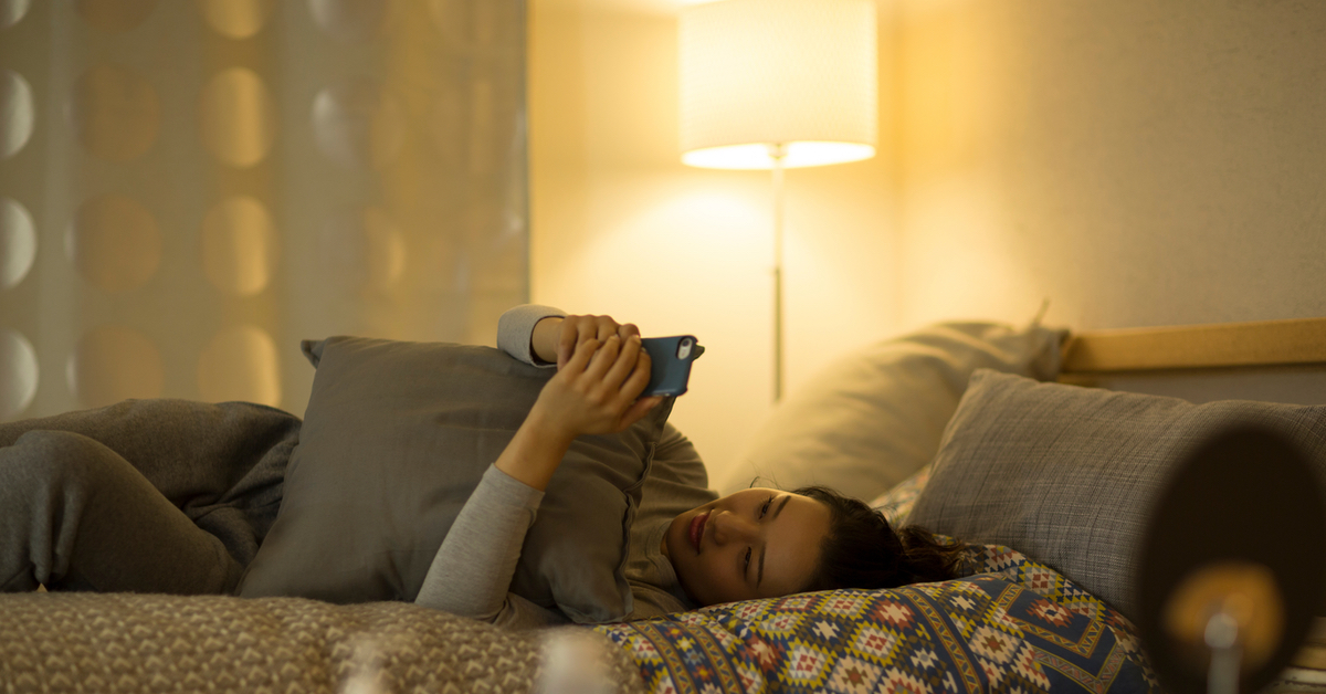 Eine Frau liegt auf dem Bett und schaut auf ihr Handy.