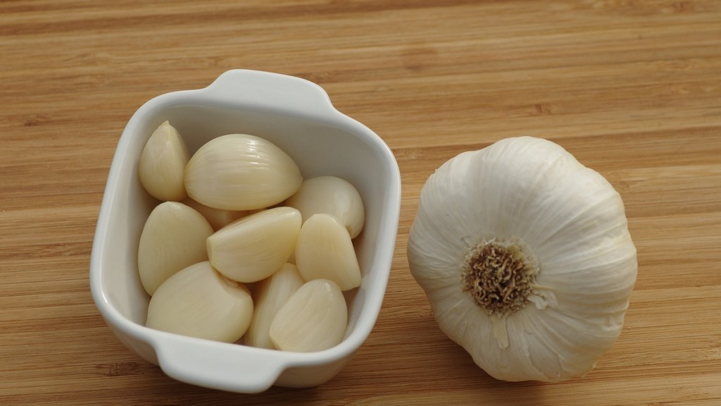 Geschälte Knoblauchzehen in einer Schale liegen neben einer Knoblauch-Knolle auf einem Brett.