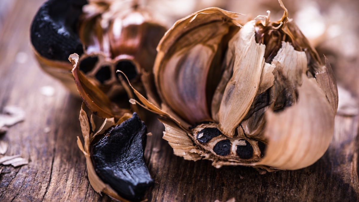 Eine Knolle schwarzer Knoblauch liegt auf einem Holzbrett.