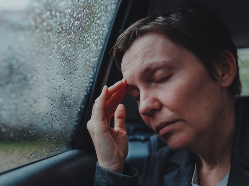 Eine Frau lehnt ihren Kopf an die Scheibe eines Autos und fest sich mit einer Hand an den Kopf.