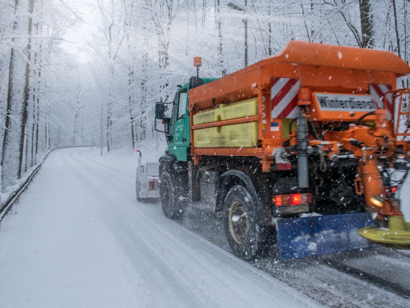 Ein Streuauto auf einer verschneiten Straße im Wald.