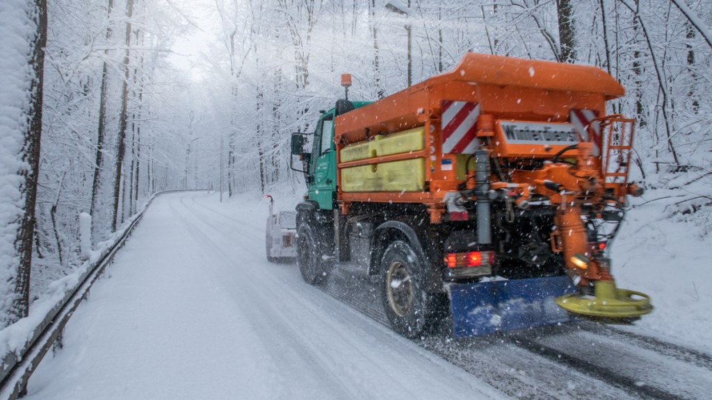 Ein Streuauto auf einer verschneiten Straße im Wald.