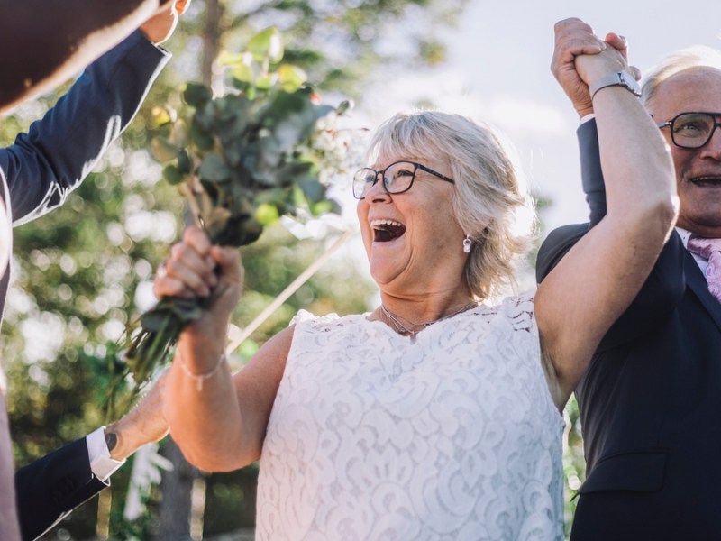 Ein älteres Hochzeitspaar jubelt zusammen mit seinen Gästen.