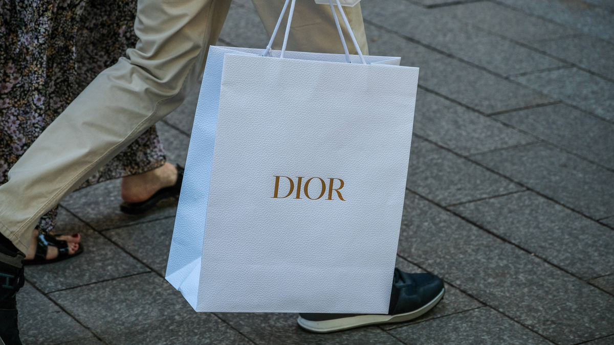 Eine Person trägt eine weiße „Dior“-Tüte.