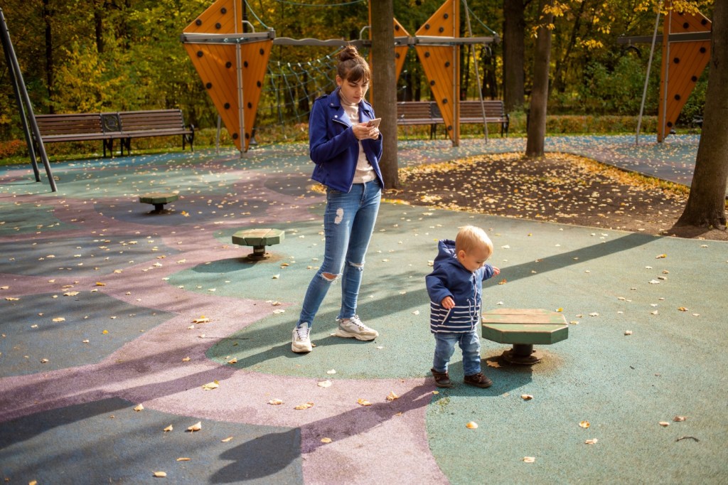 Kind auf dem Spielplatz Mutter am Handy