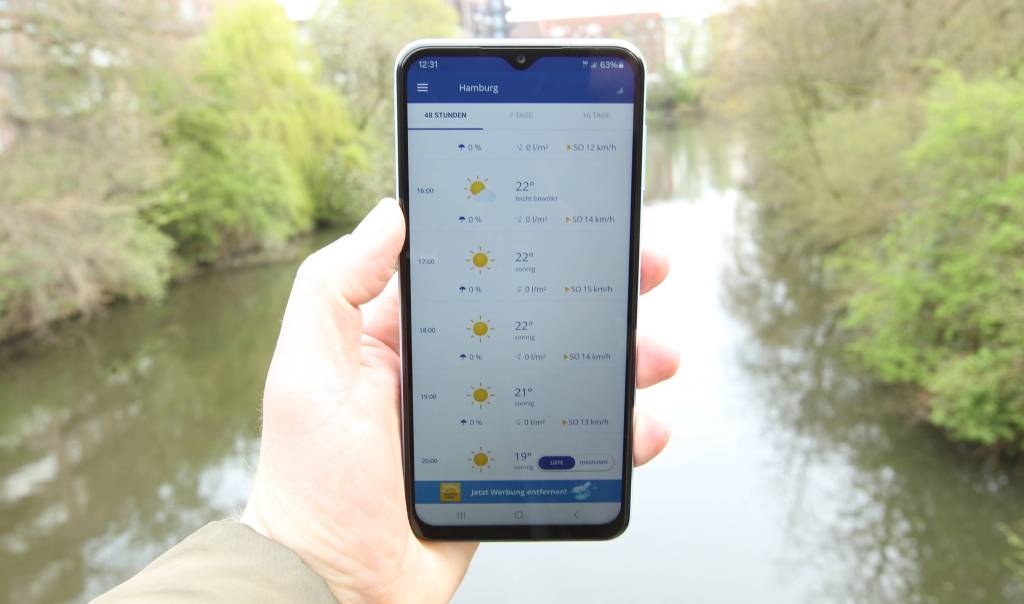 Ein Mann hält ein Smartphone mit der Wettervorhersage für Hamburg in der Hand.