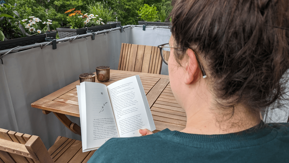 Eine Frau liest ein Buch auf einem Balkon.