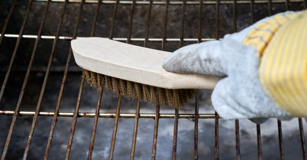 Grillrost mit einer Bürste reinigen.