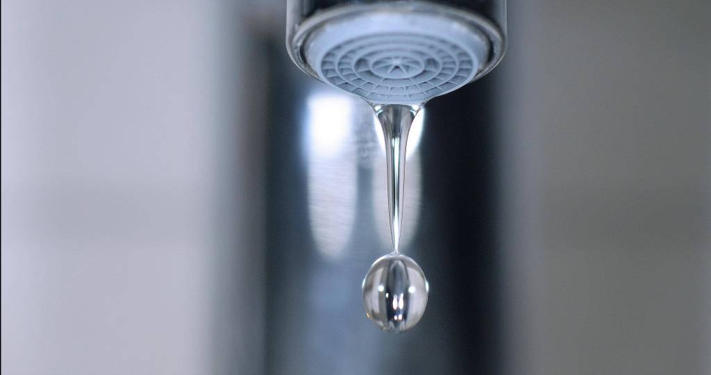 Wasser fließt aus dem Wasserhahn und bildet einen Wassertropfen.