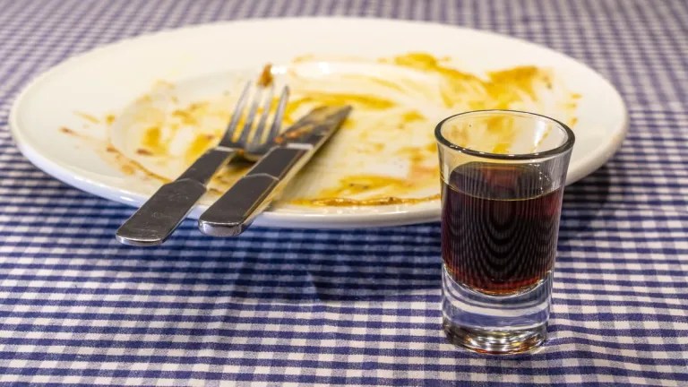 Schnapsglas vor einem leeren Teller.