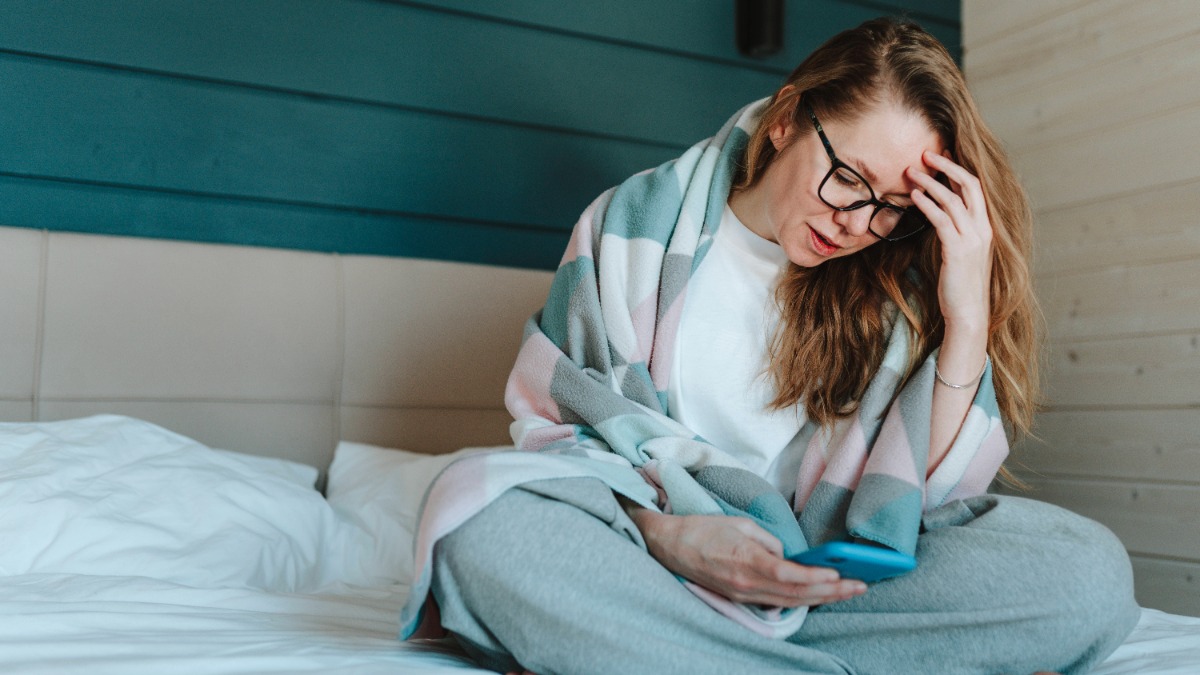 Frau sitzt auf dem Bett und hält ein Handy in der Hand