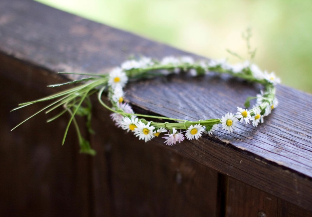 Ein Kranz aus Gänseblümchen geflochten liegt auf dem Geländer einer Veranda.