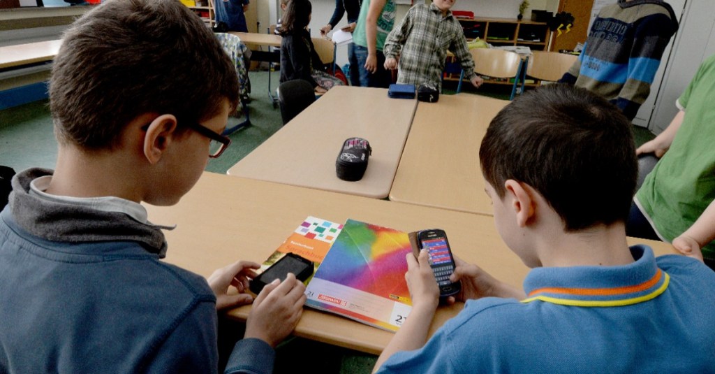 zwei Schüler benutzen ihr Handy im Unterricht