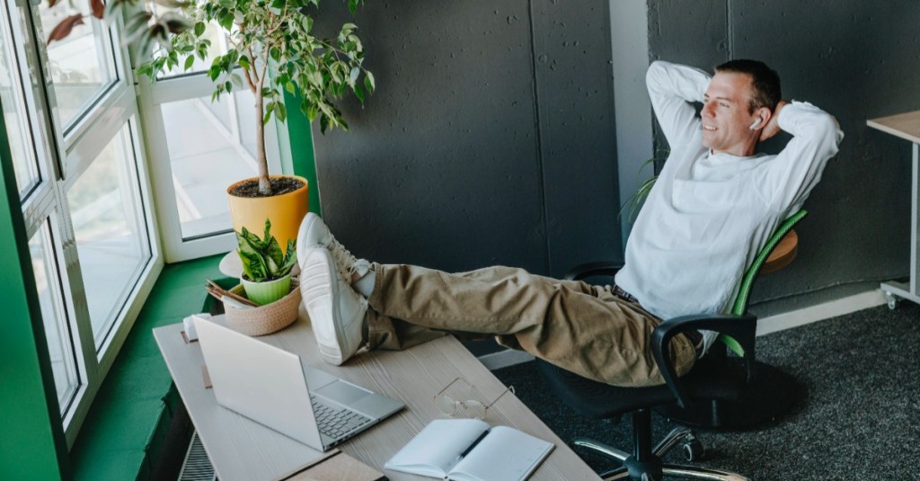 Mann sitzt relaxt mit den Beinen auf dem Tisch an seinem Arbeitsplatz und schaut in die Ferne