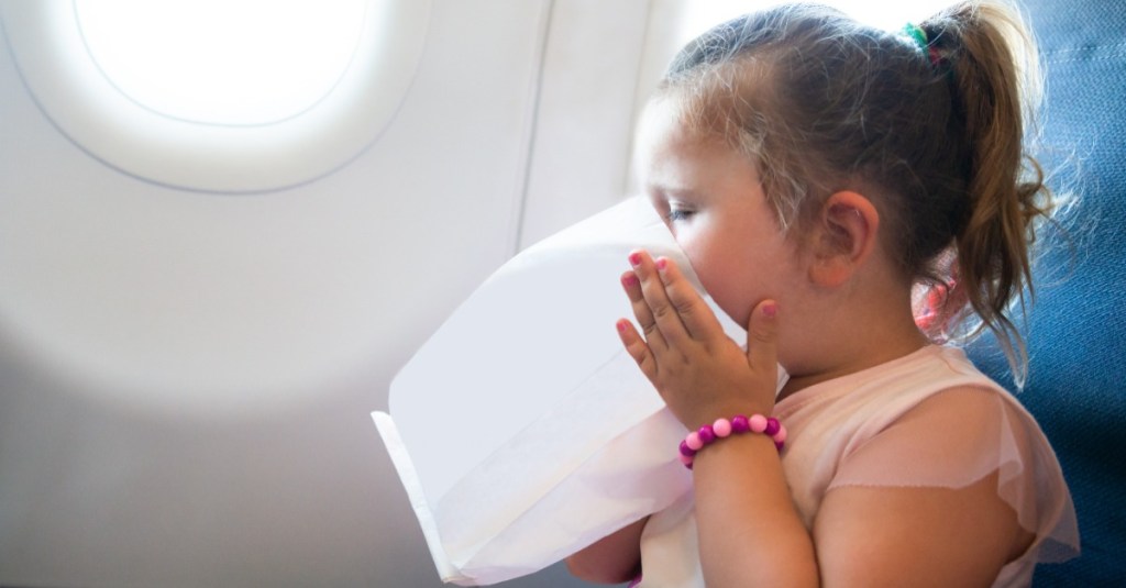 kleines Mädchen hält sich im Flugzeug Spucktüte vors Gesicht