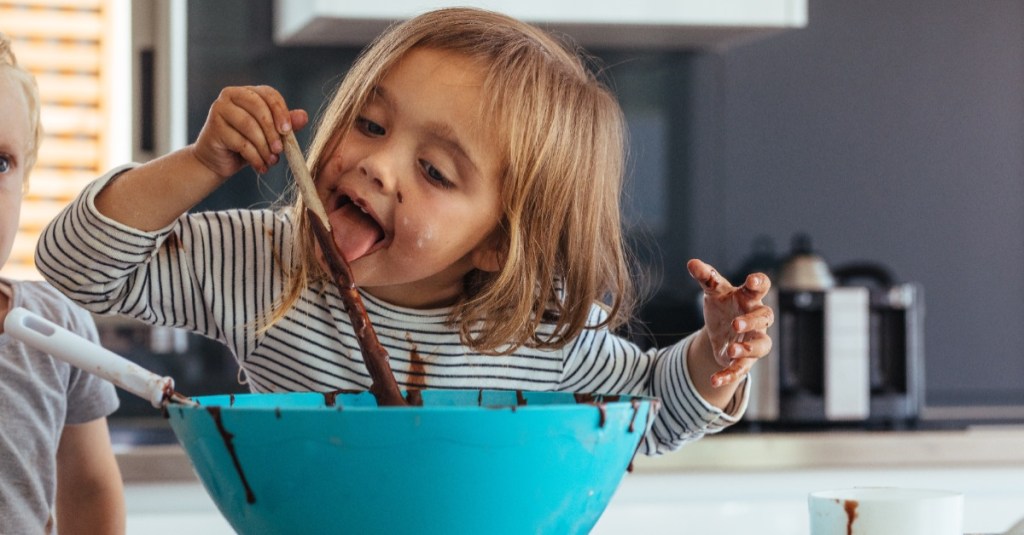 kleines Mädchen schleckt Holzlöffel mit Kuchenteig ab