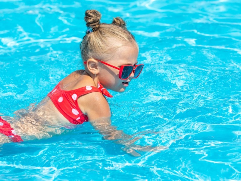 Mädchen im rosa Bikini planscht im Wasser