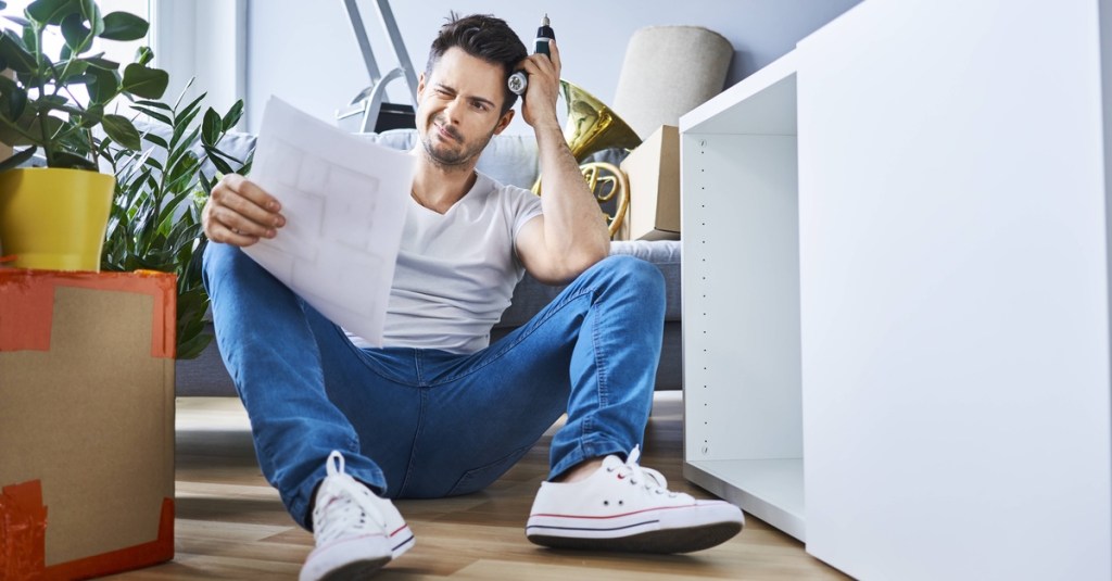 Mann sitzt auf dem Boden und versucht verzweifelt, einen Schrank aufzubauen.