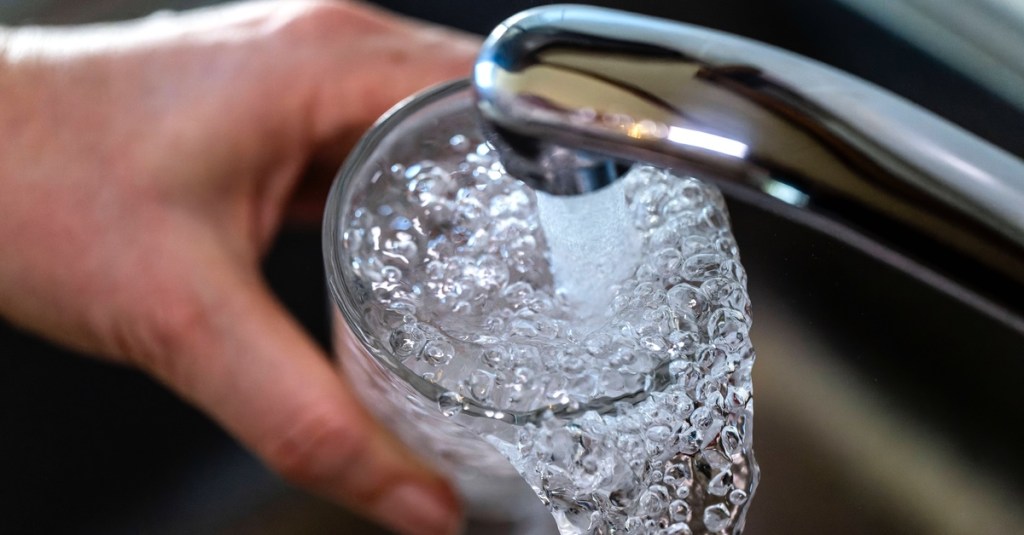 Jemand füllt ein Glas unter dem Wasserhahn mit Leitungswasser.