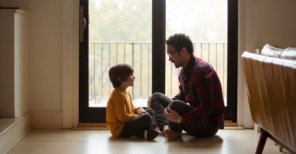 Vater und Sohn sitzen auf dem Boden vor einem Fenster und unterhalten sich