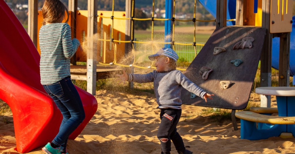 Junge wirft auf dem Spielplatz mit Sand