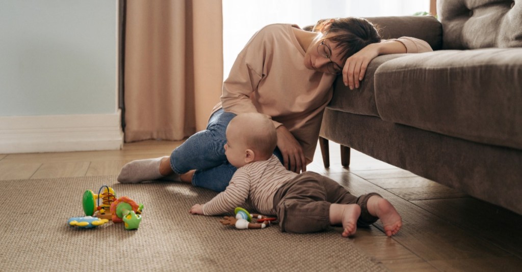 Junge Mutter lehnt erschöpft an der Couch