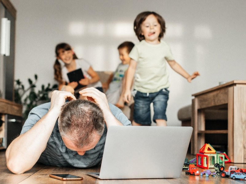 Vater versucht zu Hause am Laptop zu arbeiten, während seine Kinder im Hintergrund spielen